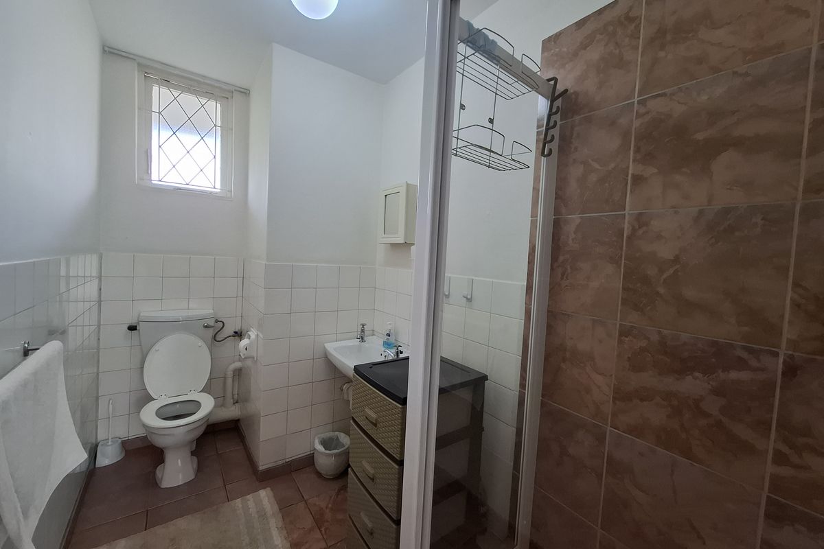A functional bathroom featuring a shower enclosure, toilet, and washbasin with tiled finishes and a leaded glass window.