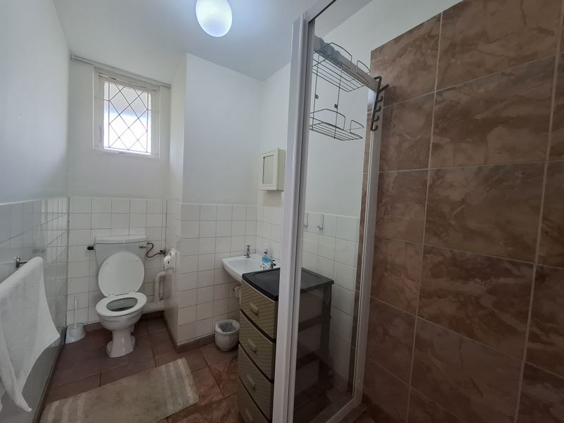 A functional bathroom featuring a shower enclosure, toilet, and washbasin with tiled finishes and a leaded glass window.