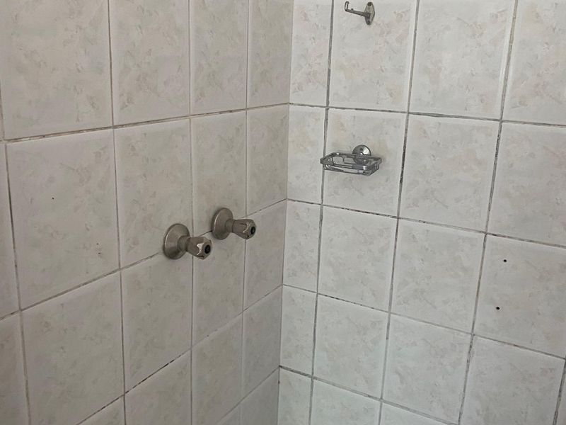 A dated shower enclosure featuring tiled walls, a fixed shower head, and integrated chrome fixtures, requiring cosmetic updates to improve its overall condition.