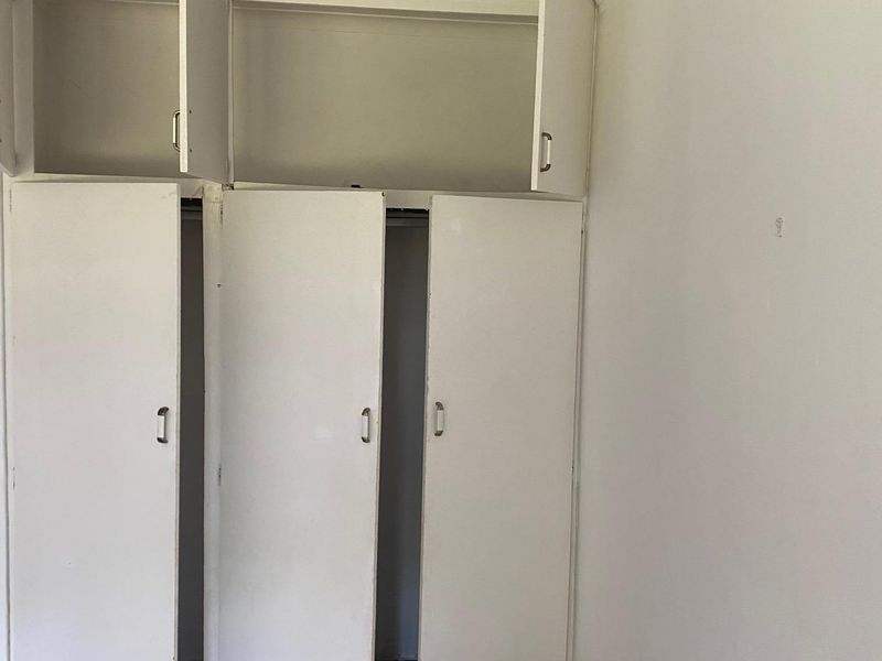 A bedroom featuring built-in cupboards with overhead storage, requiring cosmetic updates to the flooring and wall finishes.