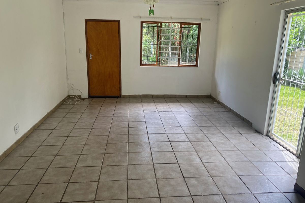An empty living room featuring tiled flooring, a ceiling fan, and a sliding glass door providing access to the garden.