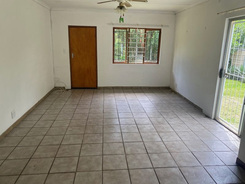 An empty living room featuring tiled flooring, a ceiling fan, and a sliding glass door providing access to the garden.
