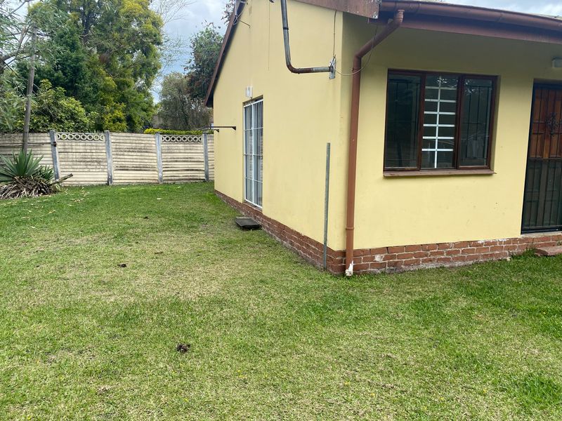 Rear view of the cottage featuring a lawn, precast boundary wall, and exterior brick plinth with security features on windows and doors.