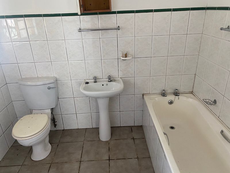 A dated bathroom featuring a pedestal basin, toilet, and bathtub with original ceramic wall and floor tiling, requiring modernization and cosmetic updates.