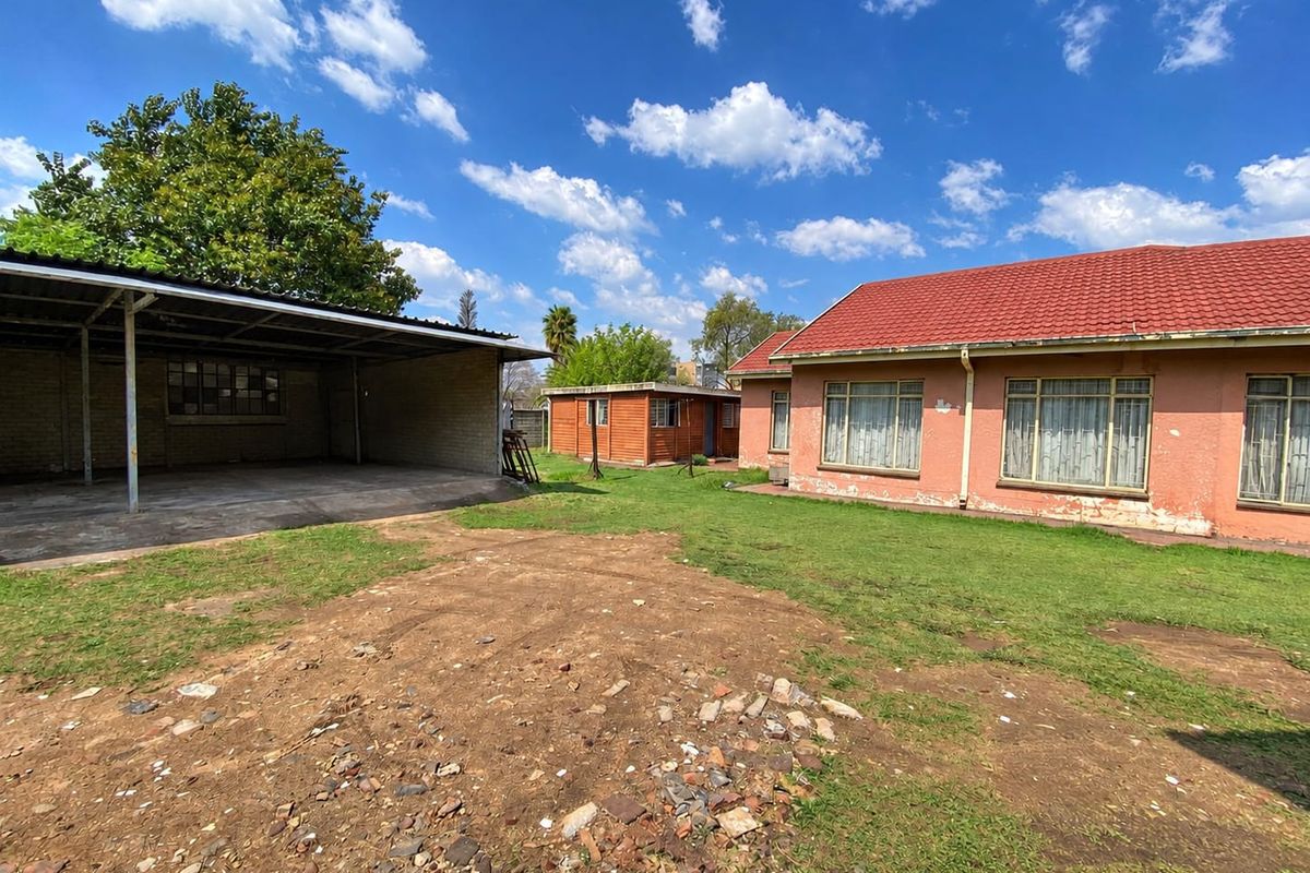 Rear view of the property featuring a large carport, a separate outbuilding, and a spacious yard with a concrete driveway and tiled roof house.