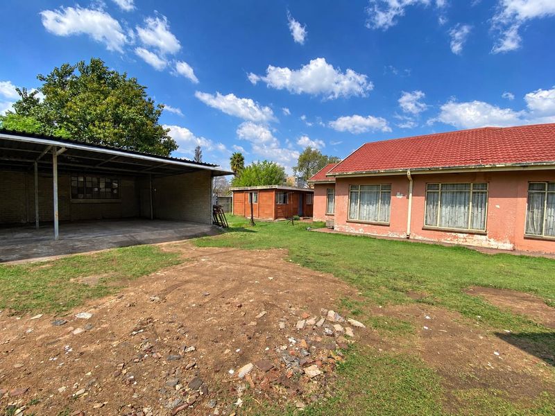 Rear view of the property featuring a large carport, a separate outbuilding, and a spacious yard with a concrete driveway and tiled roof house.