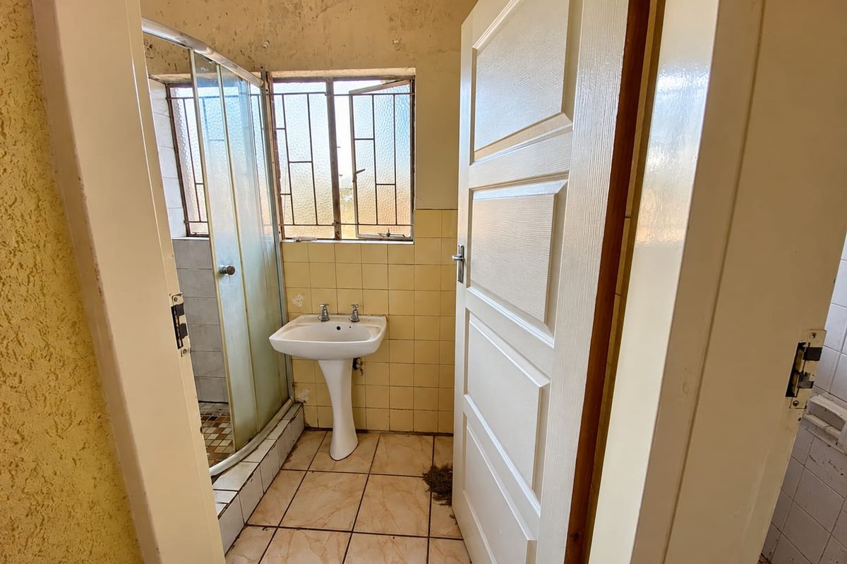 A dated bathroom featuring a pedestal basin, shower enclosure, and tiled finishes, requiring renovation to address ceiling and surface wear.