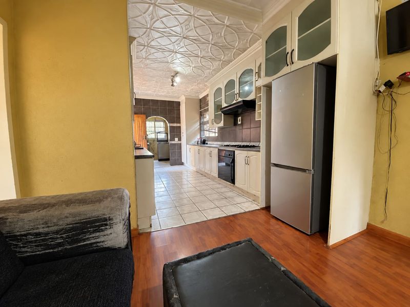 A functional kitchen featuring built-in cabinetry, tiled backsplash, and a decorative ceiling, transitioning from laminate flooring to a tiled kitchen work area.