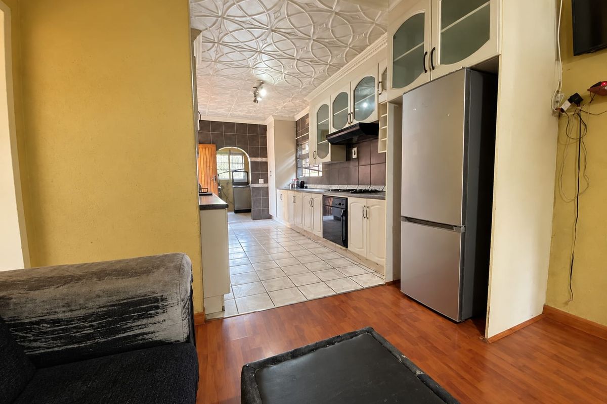 A functional kitchen featuring built-in cabinetry, tiled backsplash, and a decorative ceiling, transitioning from laminate flooring to a tiled kitchen work area.