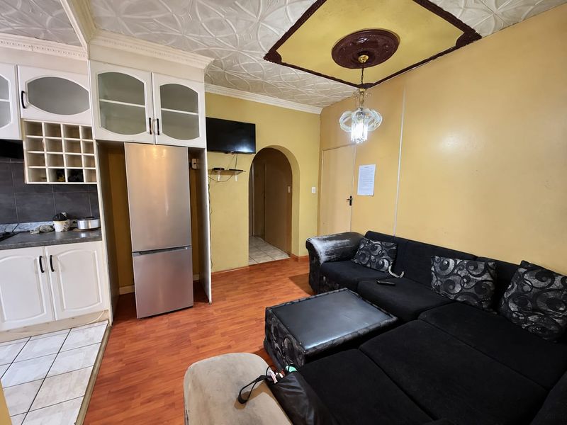 Open-plan living area featuring a compact kitchen with built-in cabinetry, laminate flooring, and decorative ceiling details, leading through an archway to other rooms.