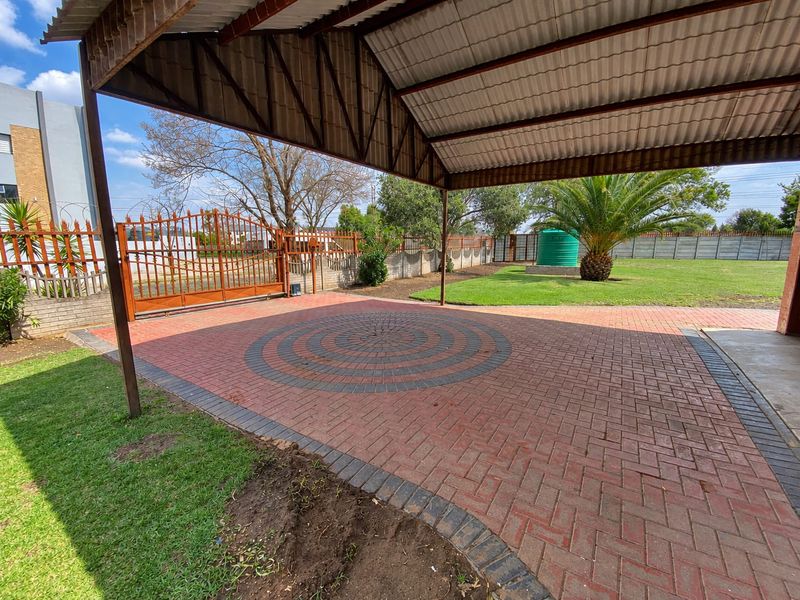 Spacious paved driveway featuring a covered carport, secure metal gate, and a well-maintained garden with a water tank.