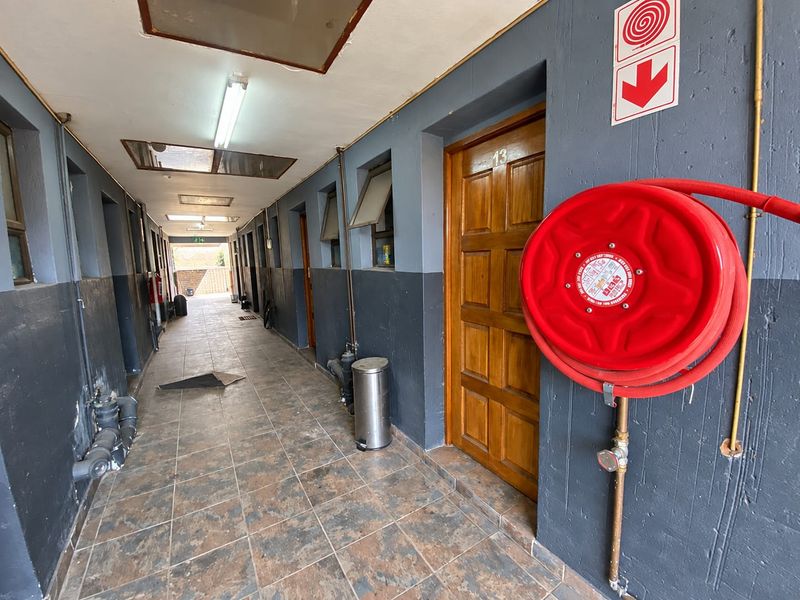 A functional apartment building hallway featuring tiled floors, timber unit doors, and essential fire safety equipment including a wall-mounted hose reel.