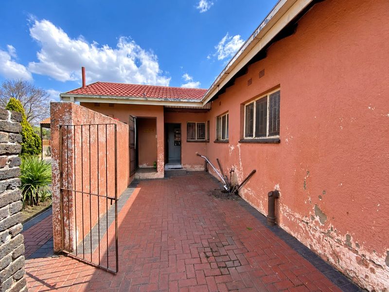Rear exterior view of the house featuring brick paving, a metal security gate, and a tiled roof, showing signs of weathered exterior wall finishes.