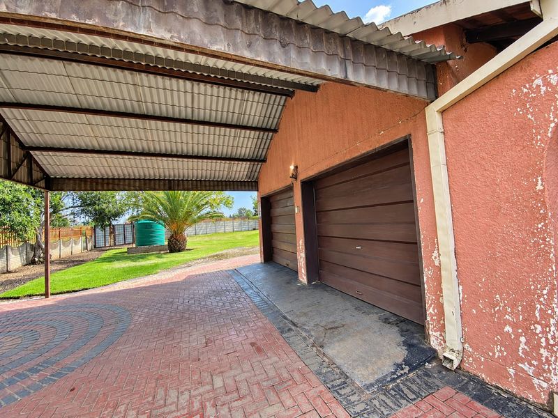 A double garage with a covered carport area, featuring paved driveway access and a rear garden with a rainwater tank.