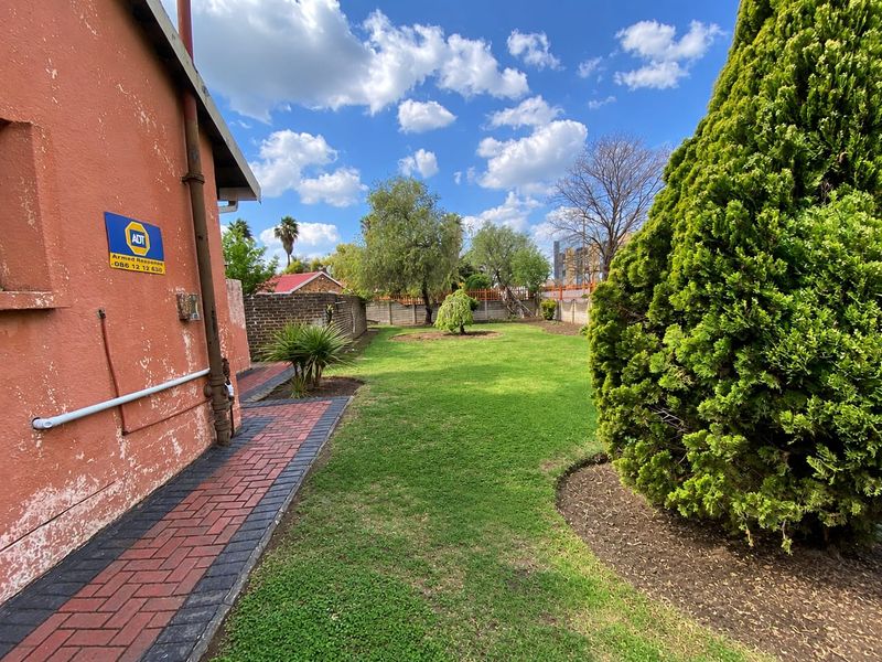 A spacious rear garden featuring a well-maintained lawn, brick paved pathway, and perimeter boundary wall.