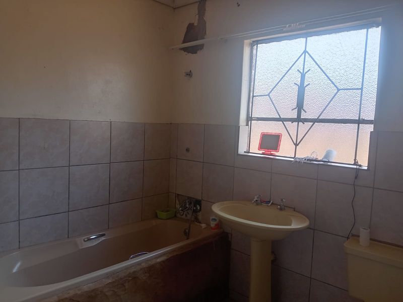 A dated bathroom featuring a pedestal basin, bathtub, and toilet, requiring renovation and repair to the wall finishes and bathtub enclosure.