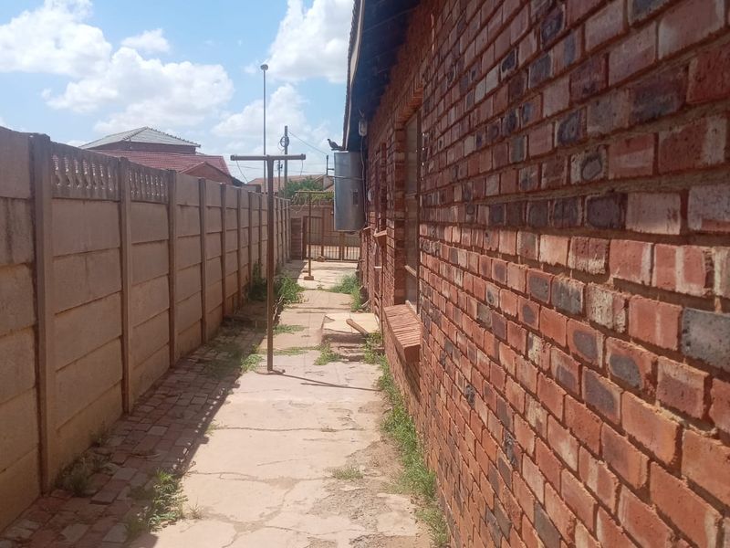 A narrow side passage featuring exposed brickwork, a precast concrete boundary wall, and a paved walkway with visible signs of wear and weathering.