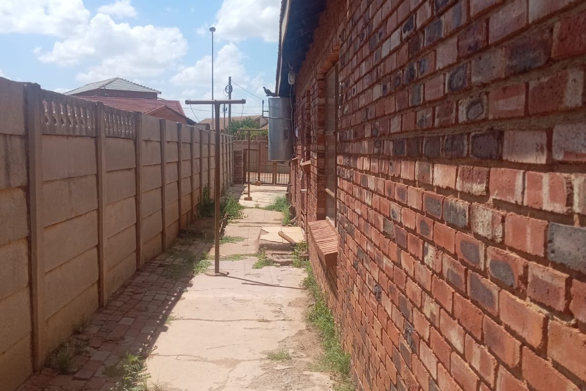 A narrow side passage featuring exposed brickwork, a precast concrete boundary wall, and a paved walkway with visible signs of wear and weathering.