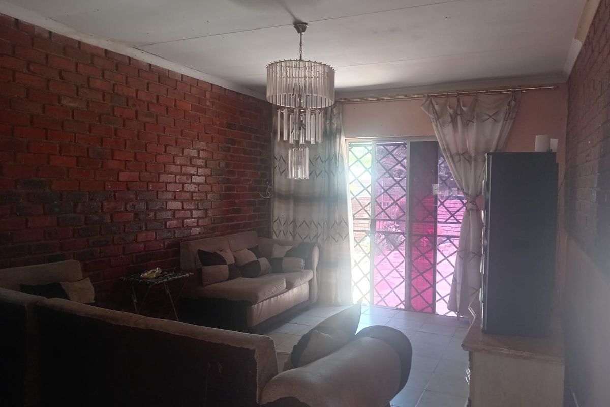 Living room featuring an exposed brick feature wall, tiled flooring, and a sliding glass door providing access to the exterior.