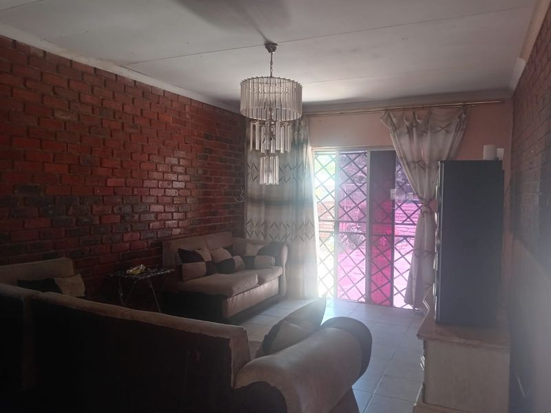 Living room featuring an exposed brick feature wall, tiled flooring, and a sliding glass door providing access to the exterior.