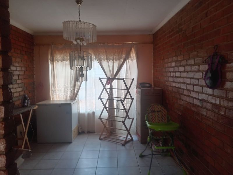 A living area featuring exposed brick walls, tiled flooring, and a decorative chandelier, offering a rustic aesthetic ready for modernization.