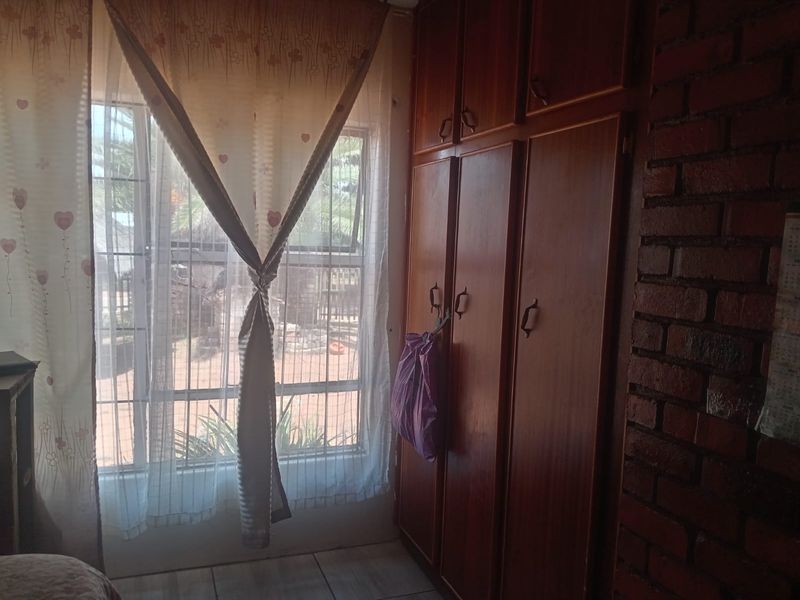 Bedroom featuring built-in wooden cupboards, an exposed brick feature wall, and a window with security bars.
