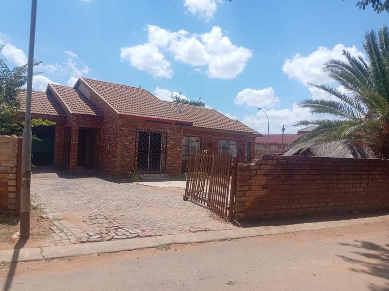 Front view of a face brick house featuring a tiled roof, paved driveway, and a brick boundary wall with a metal security gate.
