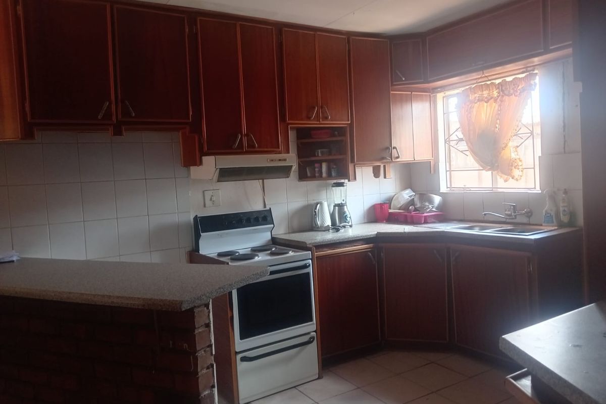 A dated kitchen featuring wooden cabinetry, a tiled backsplash, a freestanding stove with extractor fan, and a brick-based breakfast nook.
