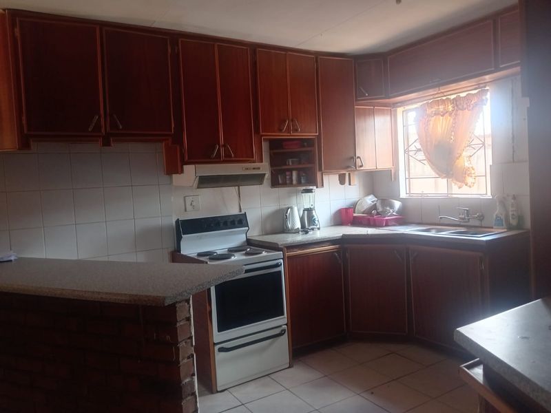 A dated kitchen featuring wooden cabinetry, a tiled backsplash, a freestanding stove with extractor fan, and a brick-based breakfast nook.