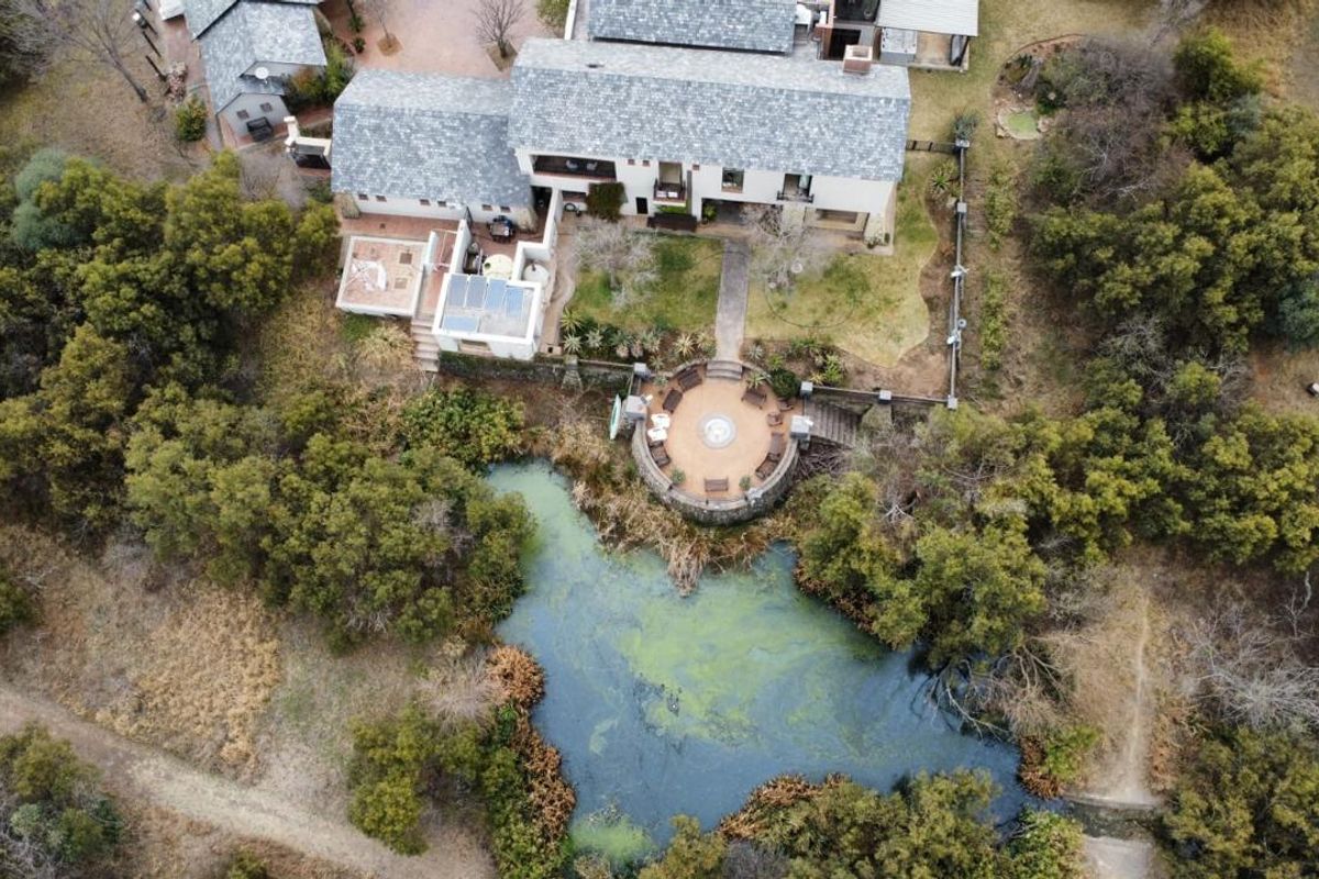 Aerial view of a large residence featuring a slate roof, solar panels, and a stone-walled circular patio overlooking a natural pond.