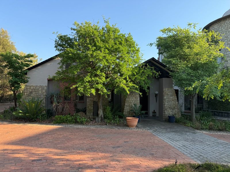 Front elevation of a house featuring stone and brick facade details, a paved driveway, and a covered entrance area with established garden landscaping.