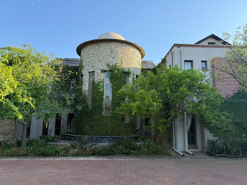 Front elevation of a unique architectural home featuring a stone-clad turret, domed roof, and brick-paved driveway entrance.