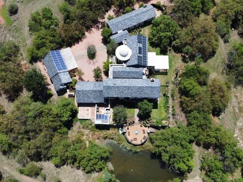 Aerial view of a sprawling property featuring multiple buildings with slate roofs, solar panels, a private pond, and landscaped grounds.