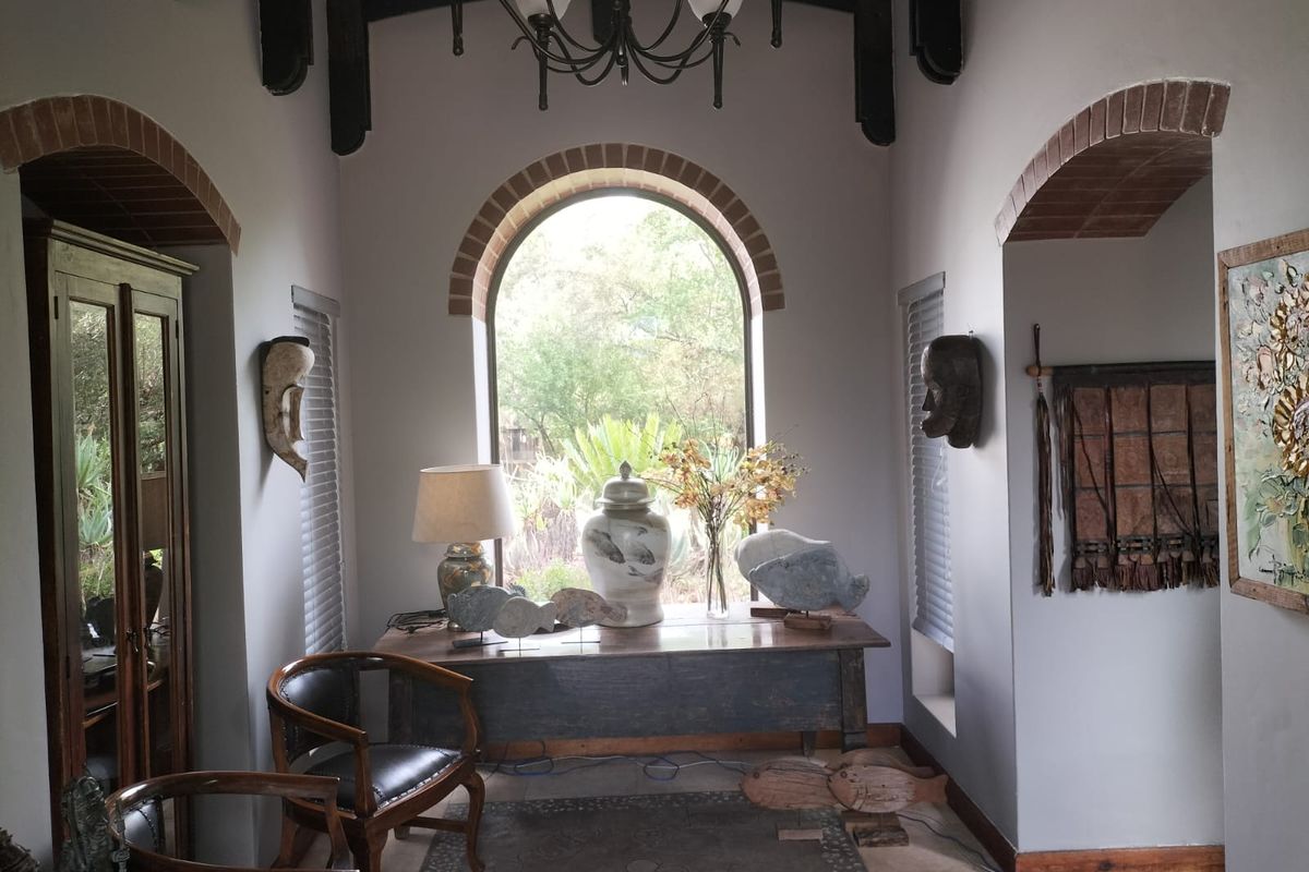 A characterful living space featuring exposed timber ceiling beams, an elegant arched window with brick detailing, and neutral tiled flooring.