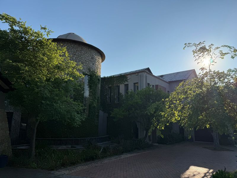 A striking architectural exterior featuring a stone turret, lush greenery, and a brick-paved driveway, showcasing unique design elements and curb appeal.