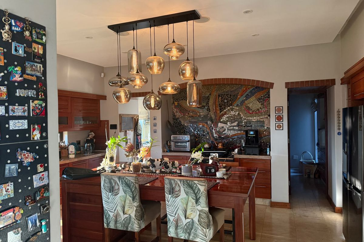 A spacious kitchen featuring warm wooden cabinetry, a unique mosaic tile backsplash, and a prominent brick archway, complemented by modern pendant lighting.