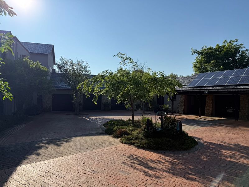 A spacious paved driveway leading to multiple garage bays, featuring stone-clad accents, mature landscaping, and roof-mounted solar panels.