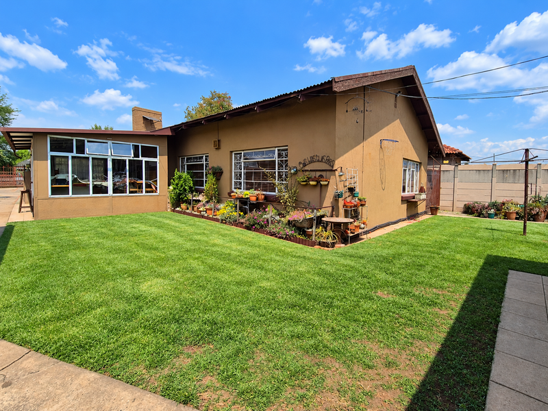 Rear view of a single-story house featuring a large lawn, enclosed patio area, and traditional plastered exterior walls with security window bars.