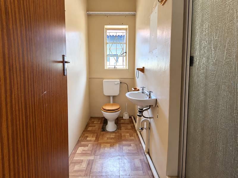 A compact bathroom featuring a wall-mounted basin, toilet, and vinyl flooring, requiring cosmetic updates to improve its dated appearance.