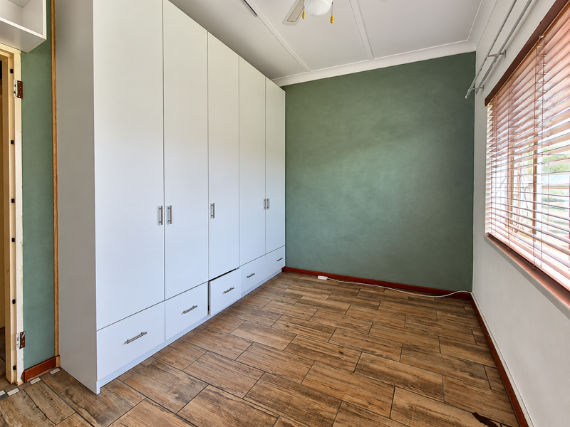 A bright, empty bedroom featuring wood-look tile flooring, a large built-in wardrobe, and a ceiling fan, with a feature green wall.