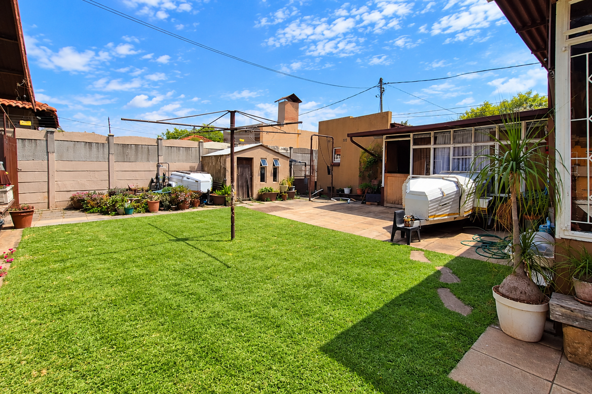 A spacious rear garden featuring a well-maintained lawn, paved patio area, precast boundary wall, and a small storage shed.