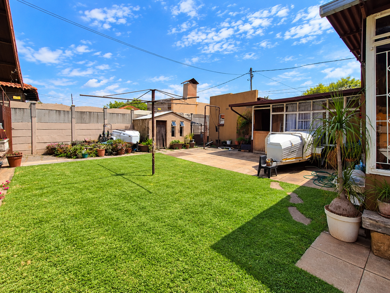 A spacious rear garden featuring a well-maintained lawn, paved patio area, precast boundary wall, and a small storage shed.