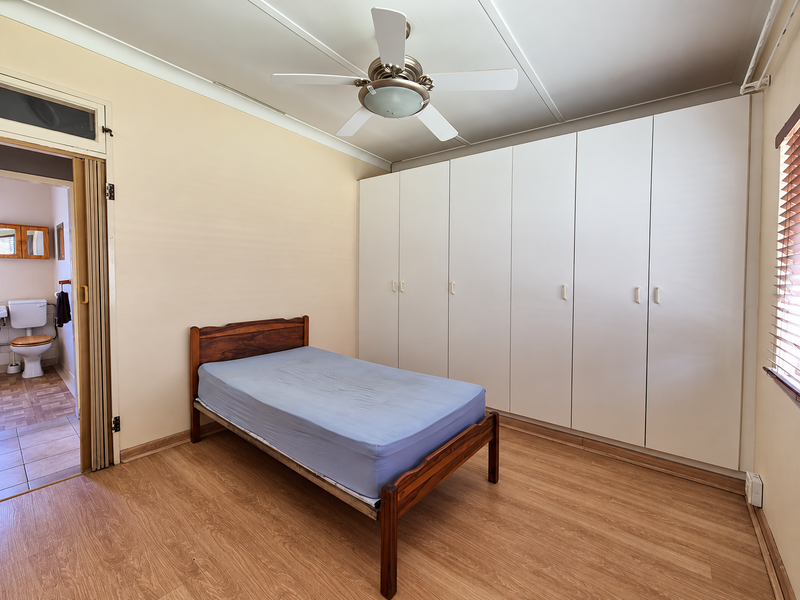 A bedroom featuring built-in wardrobes, a ceiling fan, and laminate flooring, with an adjoining bathroom visible through a folding door.