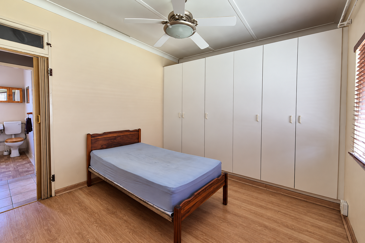A bedroom featuring built-in wardrobes, a ceiling fan, and laminate flooring, with an adjoining bathroom visible through a folding door.