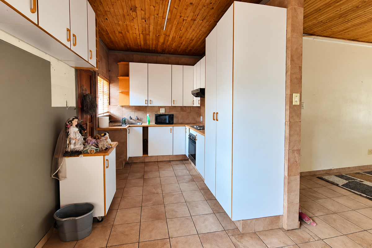 A dated kitchen featuring white cabinetry, tiled flooring, and a timber ceiling, offering a functional layout with built-in oven and extractor fan.