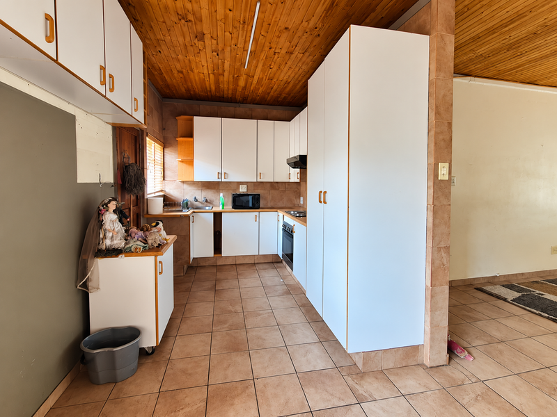 A dated kitchen featuring white cabinetry, tiled flooring, and a timber ceiling, offering a functional layout with built-in oven and extractor fan.