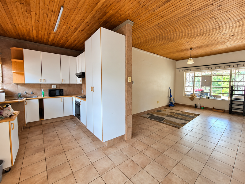 Open-plan kitchen and living area featuring tiled floors, timber ceiling, and functional built-in cabinetry with integrated oven and hob.