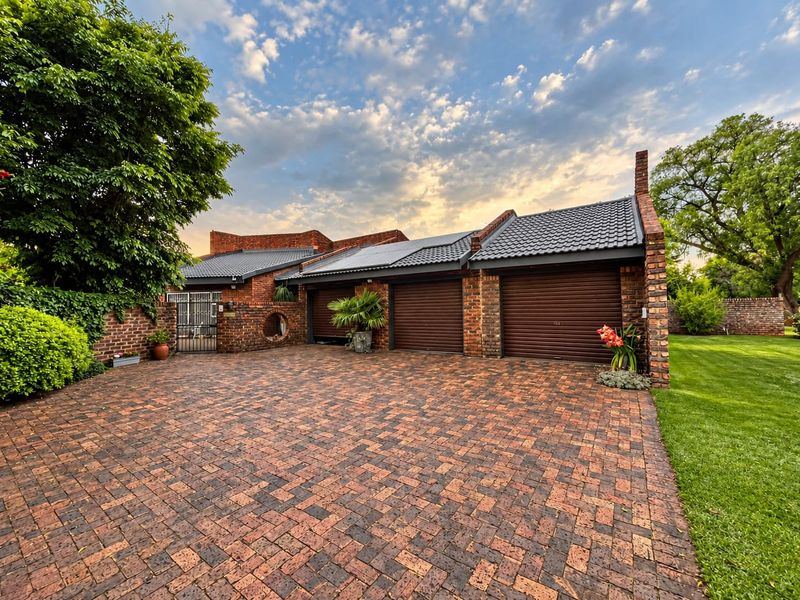 A well-maintained face brick residence featuring a spacious triple garage with roller shutter doors and an expansive brick-paved driveway.