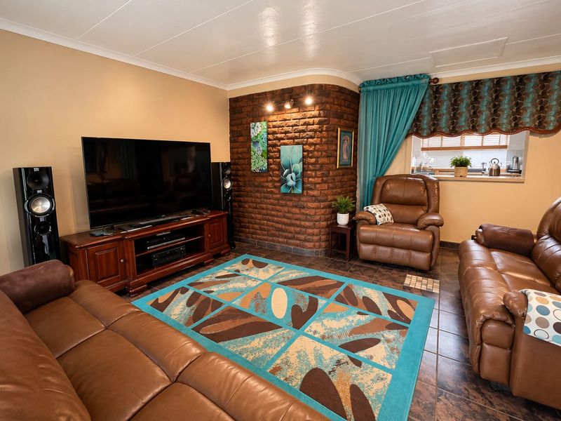 A cozy living room featuring an exposed brick accent wall, tiled flooring, and a convenient pass-through window connecting to the kitchen area.