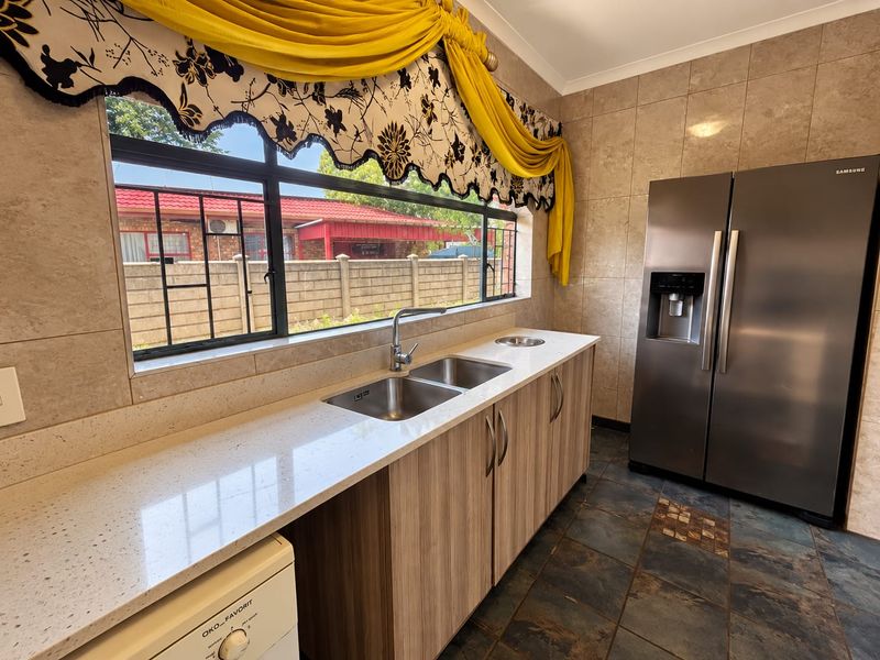 A functional kitchen featuring stone countertops, double sink, built-in cabinetry, and tiled finishes, offering a practical workspace with natural light.